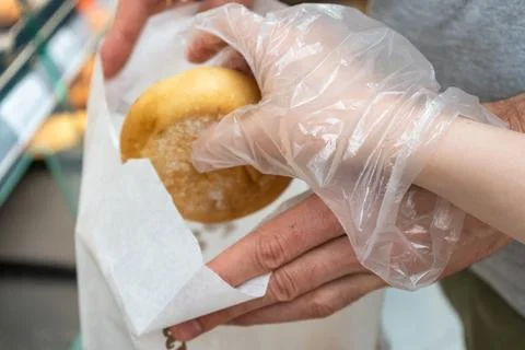 Fresh bread roll packed into paper bag by customer wearing disposable glove Foto stock
