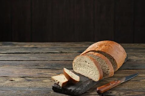 Fresh bread slice and cutting knife on rustic table Stock Photos