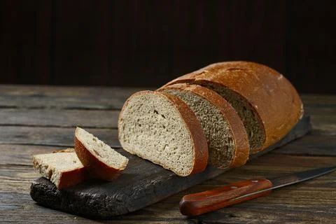 Fresh bread slice and cutting knife on rustic table Stock-Fotos