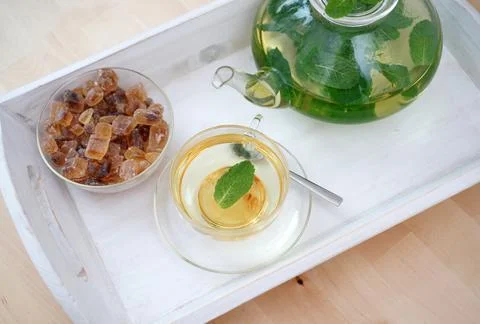 Fresh brewed mint tea on tray with teacup teapot and candi sugar healthy living Stock Photos