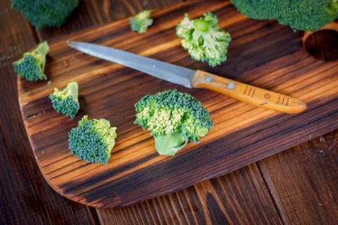 Fresh broccoli cutted on the kitchen board by knife. Stock Photos