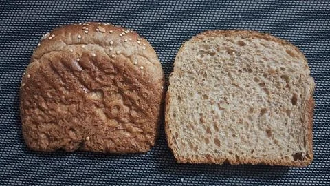 Fresh brown bread slices resting on a dark textured background surface Stock Photos