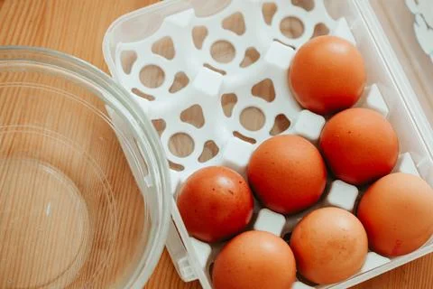Fresh brown eggs in plastic container with glass bowl on wooden table Stock Photos