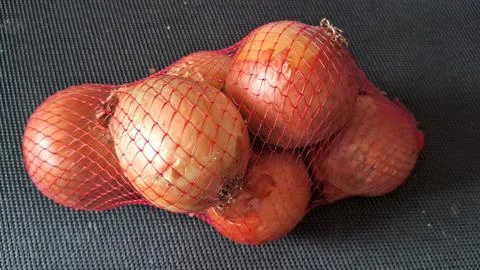 Fresh brown onions packed inside a red plastic mesh bag Stock Photos