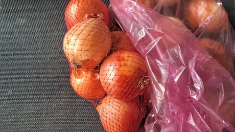 Fresh brown onions packed inside a red mesh plastic bag Stock Photos