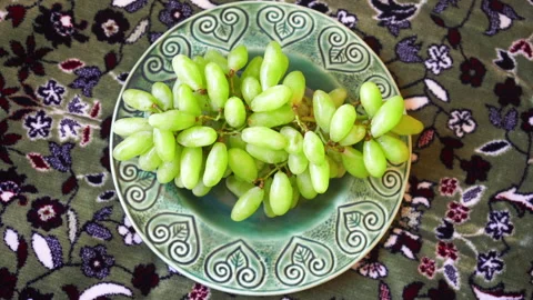 Fresh bunch of grapes on a green ceramic plate over a floral patterned rug  Stock Footage 333124625