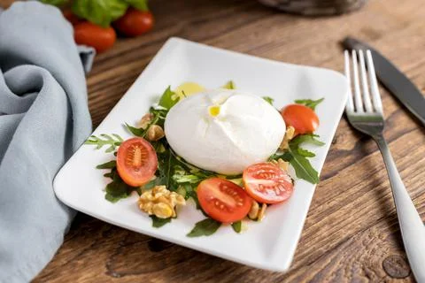 Fresh buratta cheese served with arugula leaves and cherry tomatoes in a plate Stock Photos