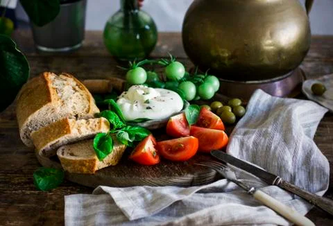 Fresh burrata cheese with tomatoes, basil and grain bread on the wooden board Stock Photos