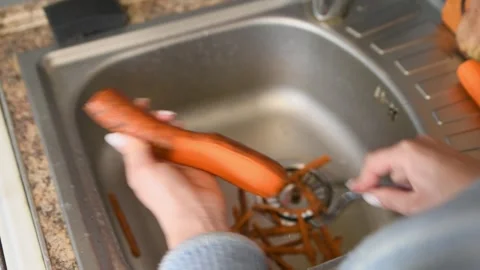 Fresh carrot peeling process with vegetable peeler over kitchen sink in nat.. Stock Footage 334956726