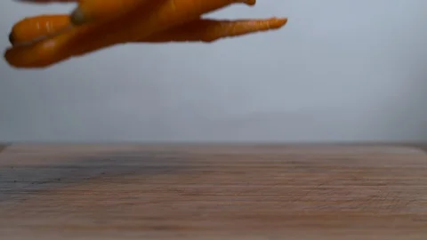 Fresh carrots falling and bouncing on the wooden surface in slow motion Stock Footage 100007714