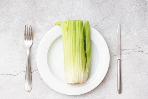 Fresh celery on a white plate with fork and knife. Background with vegan food Stock Photos