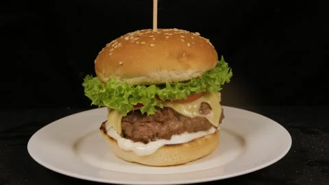 Fresh cheeseburger rotating on a white plate, isolated on black background Stock Footage 314330203
