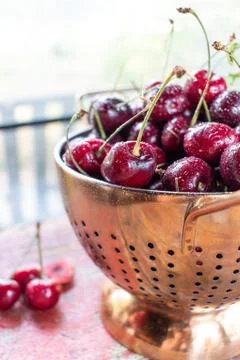 Fresh cherries in copper strainer on rustic farmhouse table Stock Photos