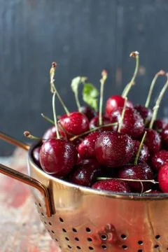Fresh cherries in copper strainer on rustic farmhouse table Stock Photos