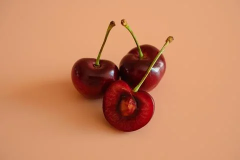 Fresh cherries with one cut open on peach background Stock Photos