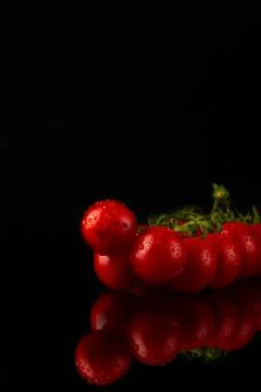 Fresh cherry tomatoes are on a mirror black table. Tomatoes with reflection Stock Photos