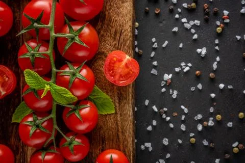 Fresh cherry tomatoes on a black background with spices. Food background. Stock Photos