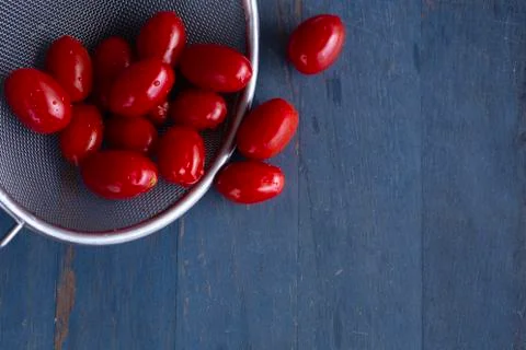 Fresh cherry tomatoes in a colander with blue wooden background, top view, co Stock Photos