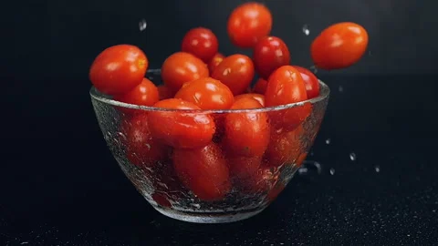 Fresh cherry tomatoes falling into wet glass bowl on black background Stock-Footage 306677941