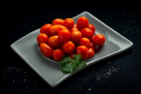 Fresh cherry tomatoes piled high on a square plate with greens Stock Photos