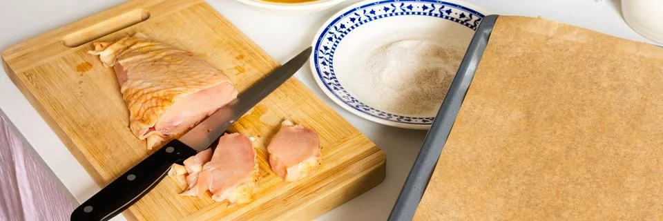 Fresh chicken is cut into pieces while a plate of flour and a bowl of batter  Stock Photos