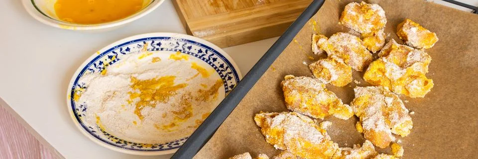 Fresh chicken is cut into pieces while a plate of flour and a bowl of batter  Stock Photos