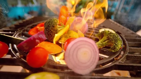 Fresh chopped vegetables tossed on hot flaming outdoor grill for healthy dinner Stock Footage 340951114
