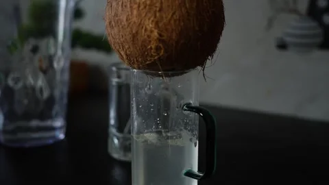 Fresh coconut dripping liquid water into a glass mug on a dark kitchen counte Stockbeeldmateriaal 339022591