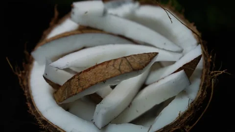 Fresh coconut slices in the brown shell on a dark background, close-up view.. Видео 339022651