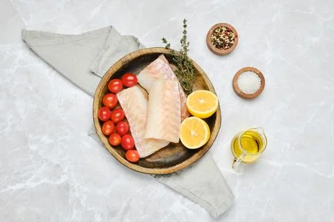 Fresh cod fillets with cherry tomatoes and lemon on a wooden plate in a bri.. Foto stock