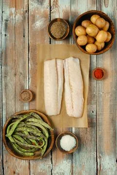 Fresh cod fish fillets with assorted vegetables and spices on a rustic wood.. Stock Photos