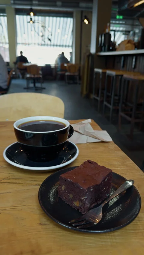 Fresh coffee cup and chocolate brownie on wooden cafe table with blurred Stock Footage 345124977