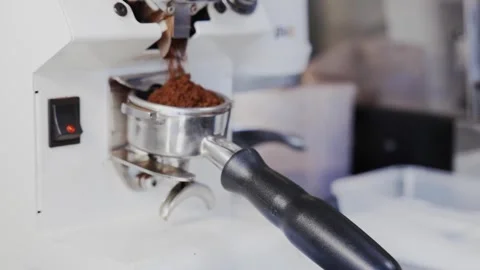Fresh coffee grounds dispense from a grinder into a portafilter, forming a Stock Footage 332614963