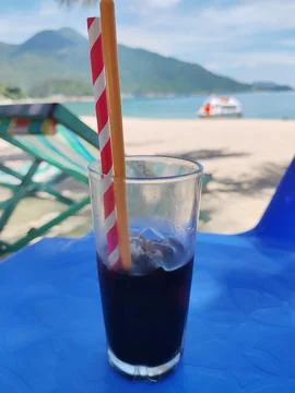 Fresh cold coffee with drinking straw on the beach in sunny day Stock Photos