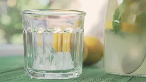 Fresh cold lemonade with mint and ice, outdoors shot. Ice falls into a glass. Video stock 166049904