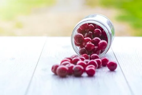 Fresh collected red cherry in a glass jar. Berries are scattered on a wooden  Stock Photos