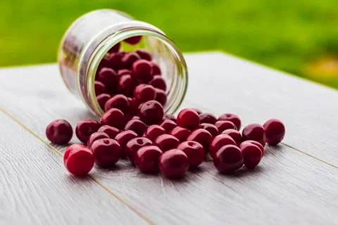 Fresh collected red cherry in a glass jar. Berries are scattered on a wooden  Stock Photos