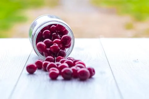 Fresh collected red cherry in a glass jar. Berries are scattered on a wooden  Stock Photos