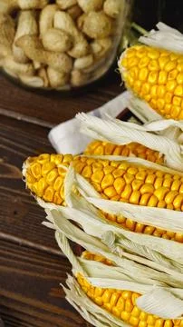 Fresh corn on the cob with husks placed beside a jar of peanuts indoors Stock Photos