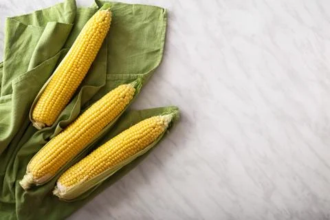 Fresh corn on cobs on marble table with green towel. Top view witn copy space Stock Photos