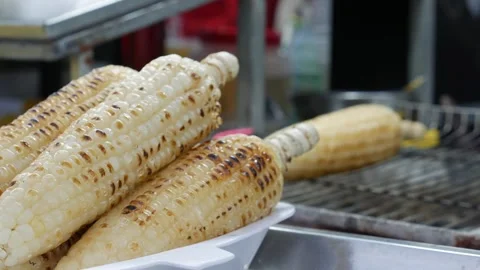 Fresh corn roasts over hot coals, filling the air with a smoky aroma at an Asian Stock Footage 314119366