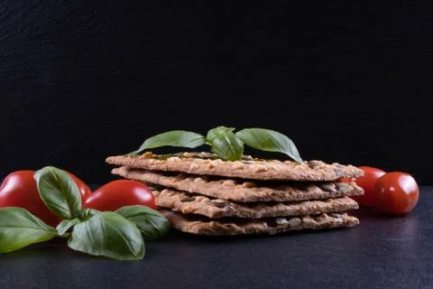 Fresh crackers, tomatoes and basil on a black stone on a table Stock Photos