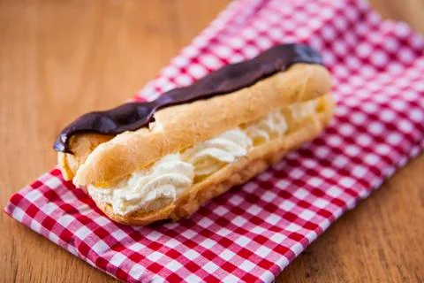 Fresh cream chocolate eclair on a red checkered cloth. Stock Photos