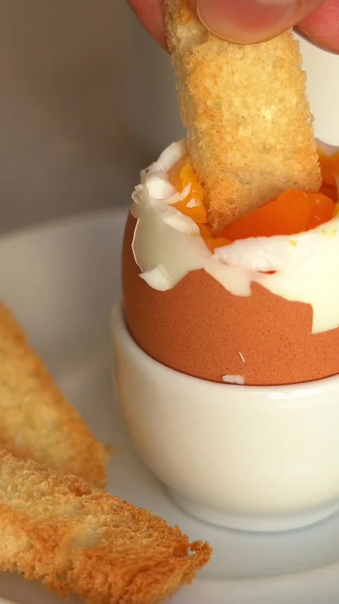 Fresh crispy bread crouton dips in soft-boiled egg in egg cup. Breakfast Stock Footage 295878135