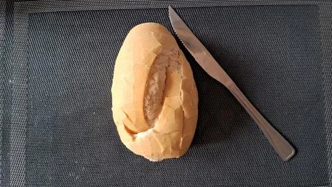 Fresh crusty bread roll placed beside a silver metal knife Stock Photos