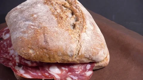 Fresh crusty ciabatta bread with sliced salami, on paper, rotating Stock Footage 331228911