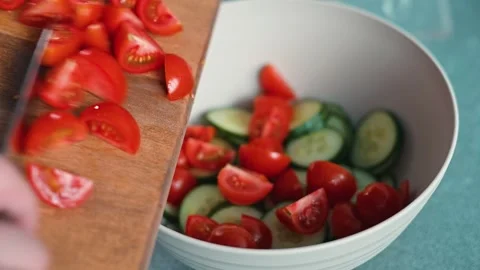 Fresh cucumbers and tomatoes are cut and combined in a large bowl. Stock Footage 338290653
