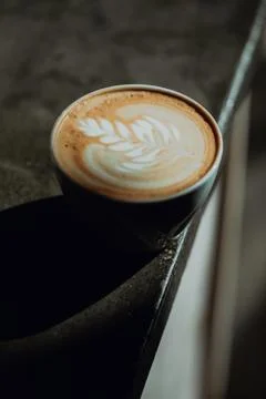 Fresh cup of latte with leaf pattern on edge of cafe counter, close up Fotos de archivo