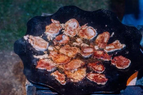Fresh cut bacon being cooked over a campfire. Stock Photos