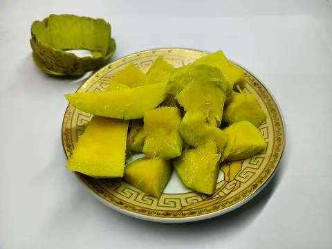Fresh cut green mango chunks on patterned plate with rolled peel. Stock Photos